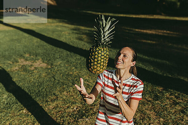 Glückliche Frau  die an einem sonnigen Tag im Park mit Ananas spielt