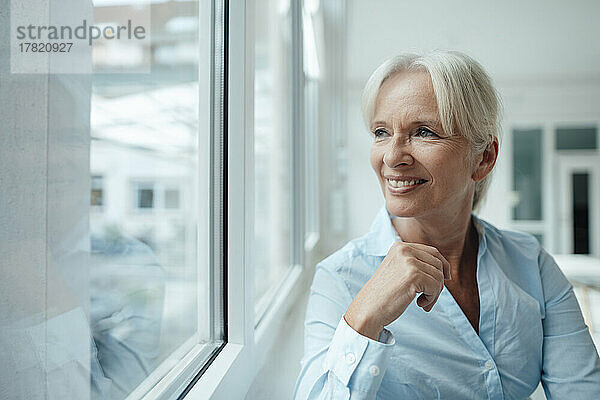 Happy senior businesswoman looking through window in office