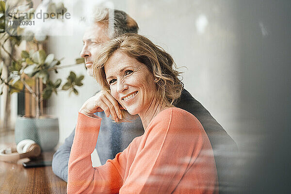 Smiling woman sitting in front of man at cafe seen through glass
