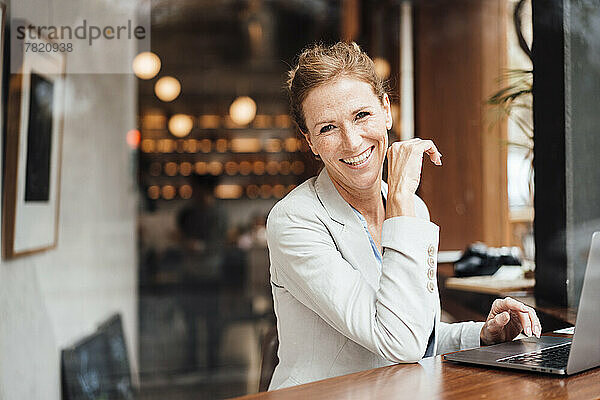 Glückliche Geschäftsfrau mit Laptop sitzt im Café