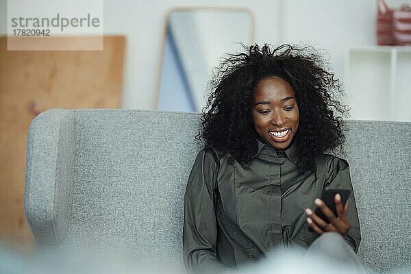 Happy byoung woman holding smart phone sitting on sofa