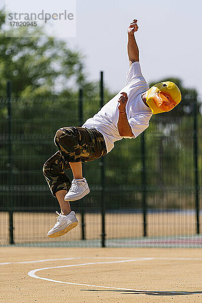 Mann mit Tiermaske springt an sonnigem Tag auf Sportplatz