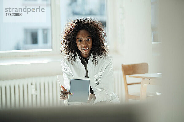 Lächelnde Ärztin mit lockigem Haar zeigt auf Tablet-PC
