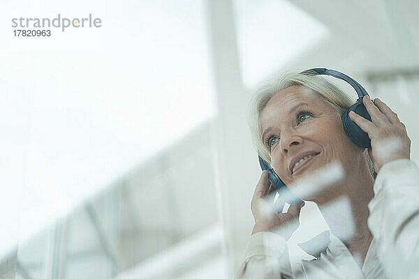 Lächelnde ältere Frau  die durch Glas gesehen Musik hört