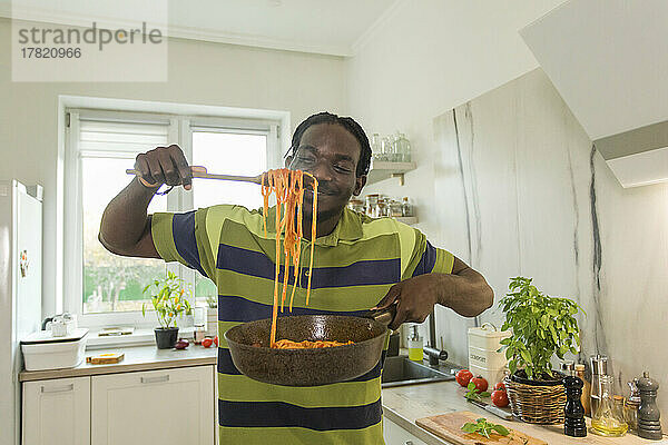 Lächelnder Mann hält einen Topf Spaghetti in der Küche