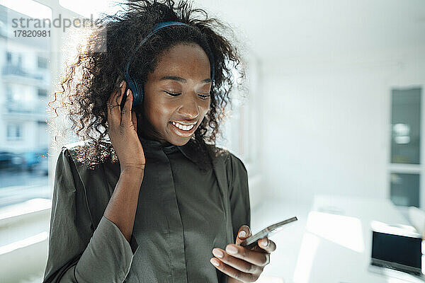 Lächelnde junge Frau  die ihr Smartphone nutzt und über drahtlose Kopfhörer Musik hört