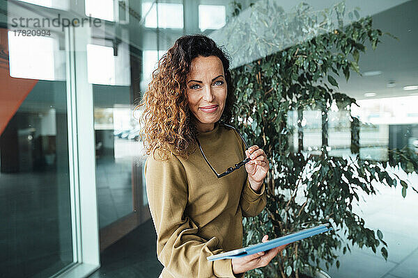 Lächelnde Frau mit Brille und Tablet-PC am Arbeitsplatz