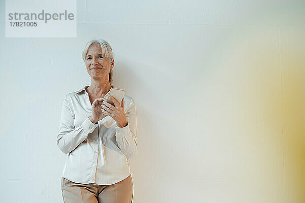 Smiling businesswoman holding mobile phone standing against white background
