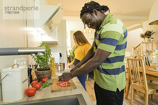 Lächelnder Mann schneidet Tomaten von seiner Freundin in der heimischen Küche