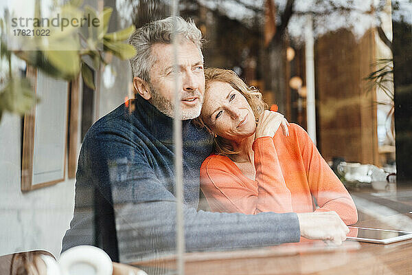 Mann umarmt Frau  die im Café sitzt und durch Glas gesehen wird