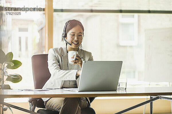 Glückliche Geschäftsfrau mit Headset  die im Büro am Laptop arbeitet