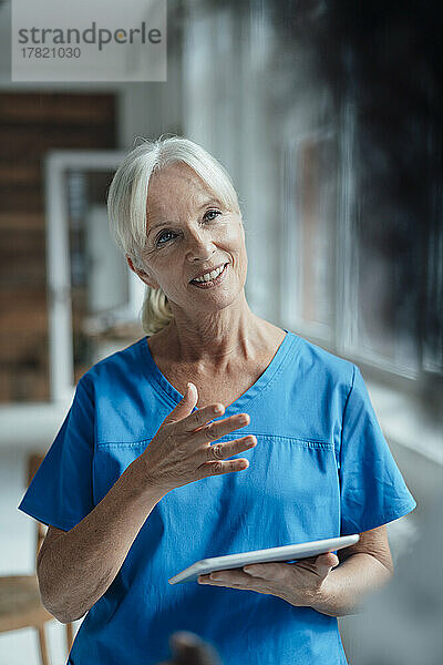 Lächelnde Krankenschwester hält gestikulierend einen Tablet-PC in der Hand