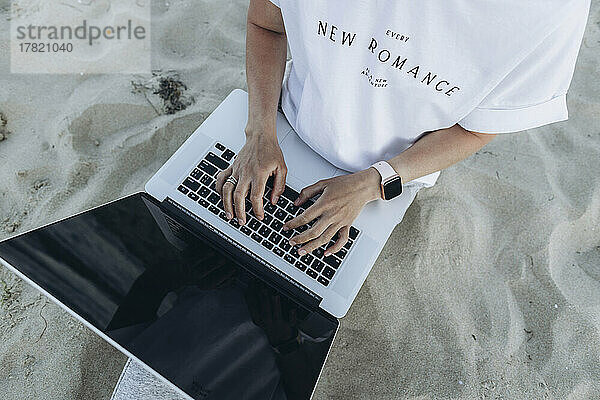 Frau sitzt mit Laptop im Sand am Strand