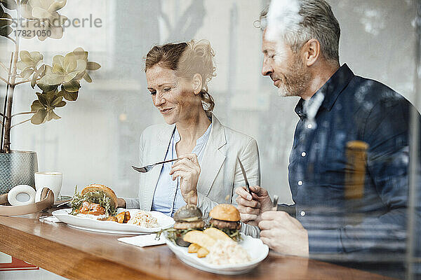 Lächelnde Geschäftsfrau mit Geschäftsmann beim Mittagessen im Café durch Glas gesehen
