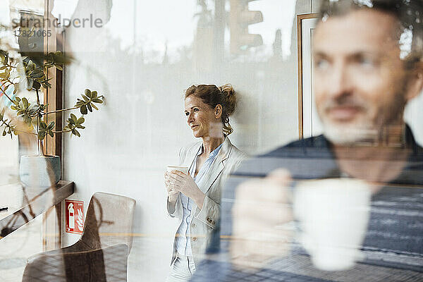 Geschäftsmann und Geschäftsfrau halten Kaffeetasse im Café  gesehen durch Glas