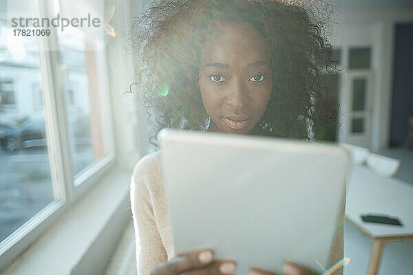 Junge Geschäftsfrau mit lockigem Haar hält Tablet-PC im Büro