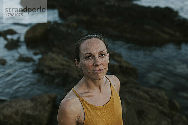 Lächelnde Frau vor einem Felsen am Meeresufer
