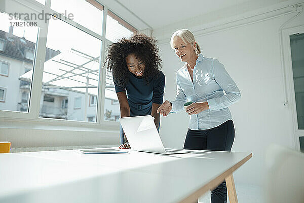 Glückliche Geschäftsfrauen diskutieren am Laptop am Schreibtisch im Büro