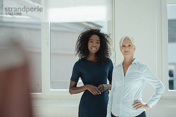 Lächelnde Geschäftsfrau mit der Hand auf der Hüfte  die neben ihrem Kollegen im Büro steht