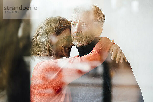 Glückliche Frau umarmt Mann im Café  gesehen durch das Fenster