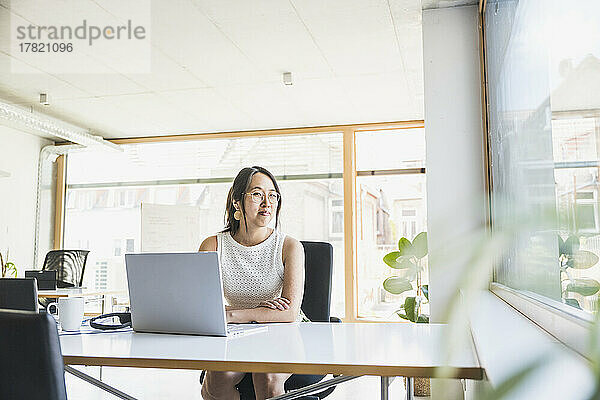 Lächelnde Geschäftsfrau mit Laptop auf dem Schreibtisch im Büro