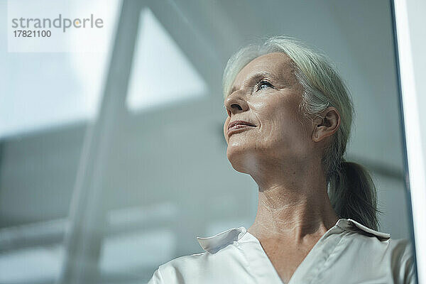 Thoughtful senior businesswoman seen through glass