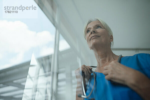 Nachdenkliche Krankenschwester mit Stethoskop am Fenster