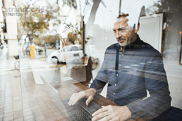Businessman using laptop in cafe seen through glass