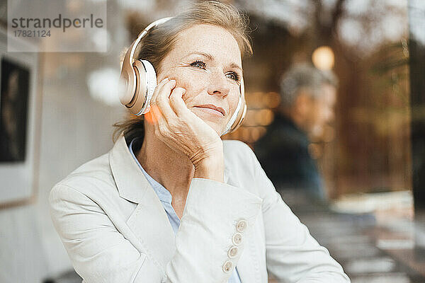 Lächelnde Geschäftsfrau  die im Café Musik über drahtlose Kopfhörer hört