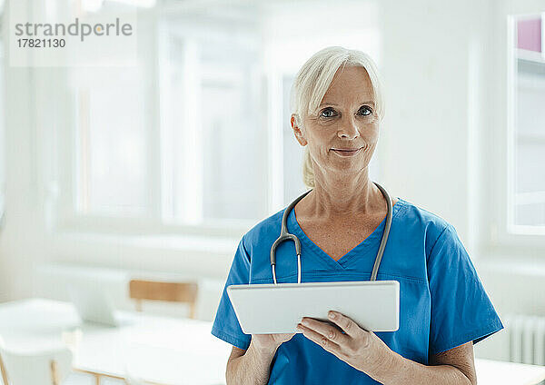 Smiling senior doctor holding tablet PC