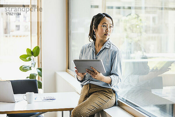 Geschäftsfrau mit Tablet-PC schaut durchs Fenster