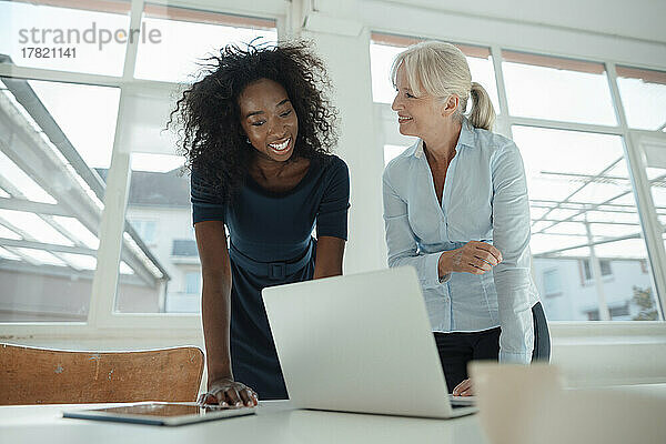 Lächelnde Geschäftsfrauen diskutieren am Laptop am Schreibtisch im Büro