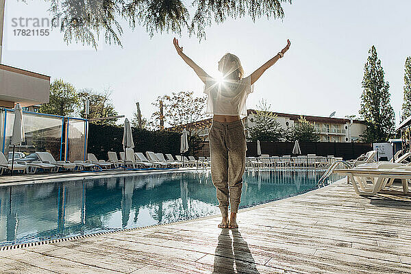 Frau mit erhobenen Armen steht an einem sonnigen Tag am Schwimmbad