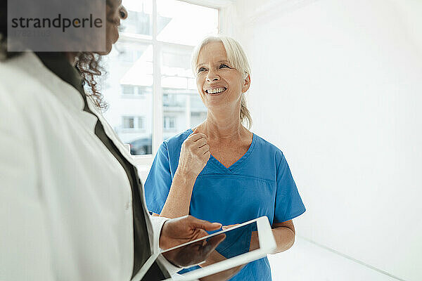 Lächelnde Krankenschwester im Gespräch mit einer Ärztin  die einen Tablet-PC hält