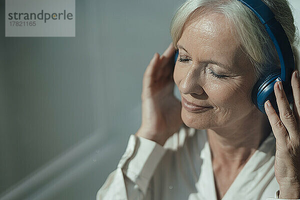 Lächelnde ältere Frau mit geschlossenen Augen  die Musik über kabellose Kopfhörer genießt