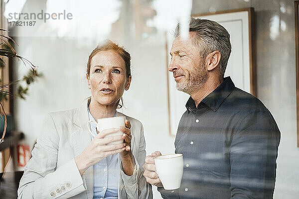 Geschäftsfrau mit Geschäftsmann hält Kaffeetasse im Café  gesehen durch Glas