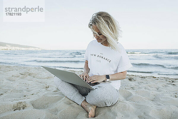 Glückliche Frau benutzt Laptop am Strand