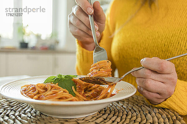Hände einer Frau  die zu Hause eine Gabel mit Spaghetti hält
