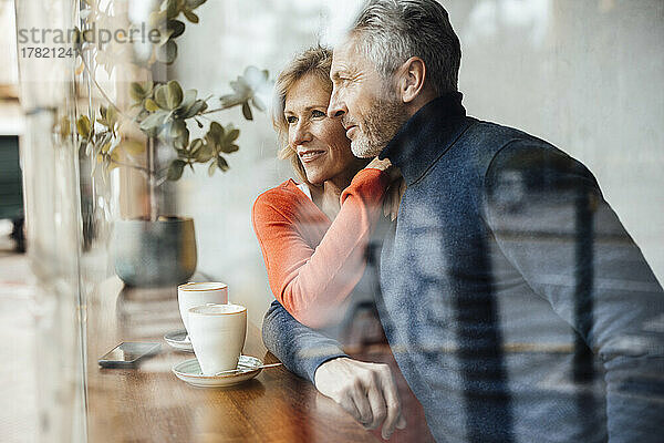 Lächelndes Paar sitzt im Café und sieht durch Glas