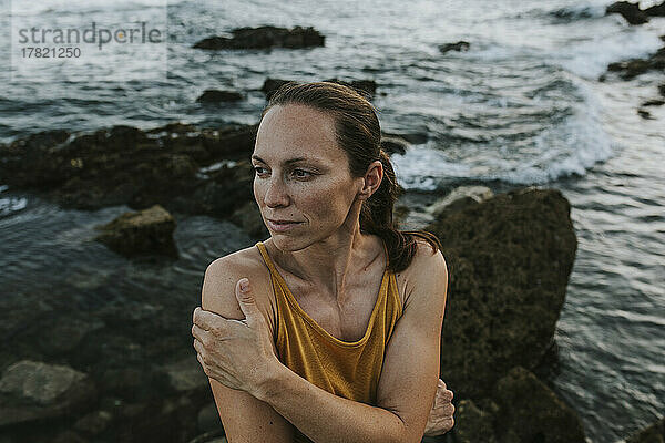 Nachdenkliche Frau umarmt sich am Meeresufer