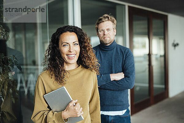 Lächelnde Geschäftsfrau mit digitalem Tablet und Kollege im Büro