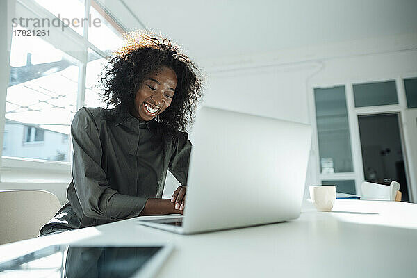 Glückliche Geschäftsfrau sitzt mit Laptop am Schreibtisch im Büro