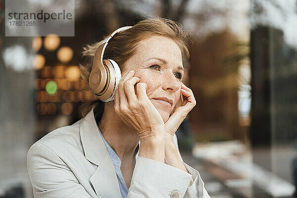 Geschäftsfrau mit Kopf in den Händen  die im Café Musik über drahtlose Kopfhörer hört
