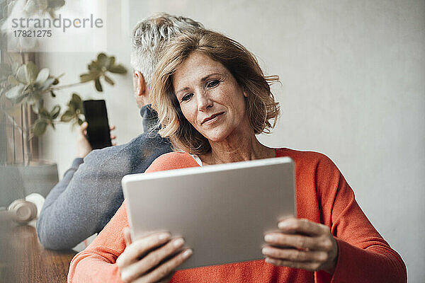 Frau mit Tablet-PC sitzt vor Mann im Café