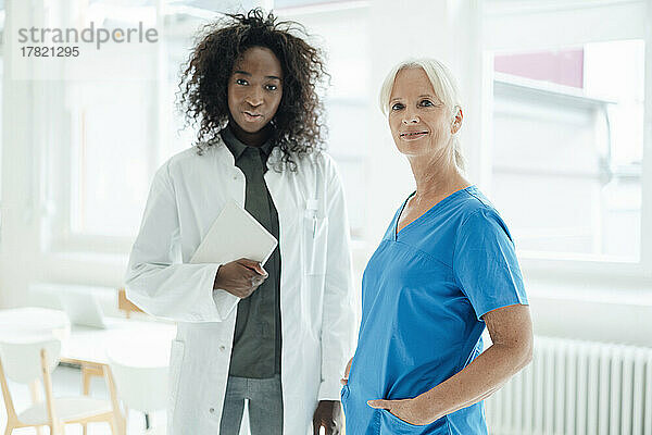 Nurse with hands in pockets standing by female doctor holding tablet PC