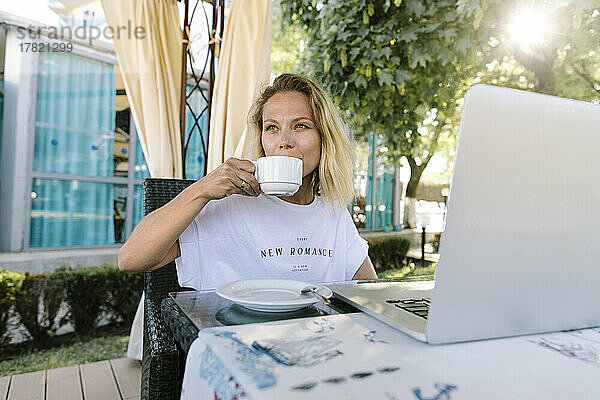 Freiberufler trinkt Kaffee und sitzt mit Laptop am Tisch im Resort