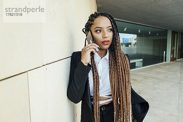 Junge Geschäftsfrau spricht mit Smartphone und lehnt an der Wand