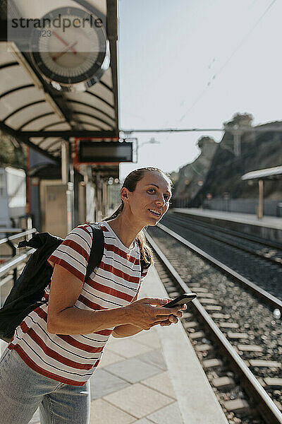 Lächelnde Frau mit Telefon wartet am Bahnsteig