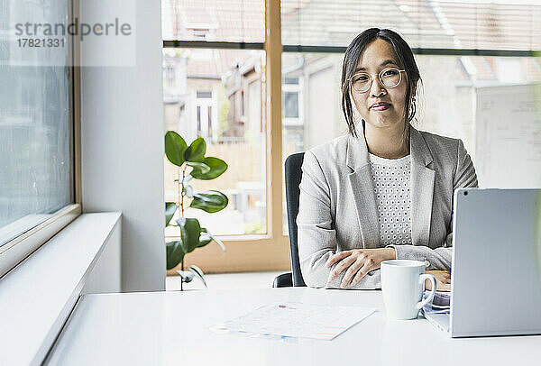 Lächelnde Geschäftsfrau sitzt am Schreibtisch im Büro