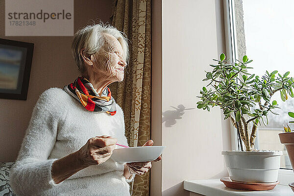 Ältere Frau mit Schüssel am Fenster